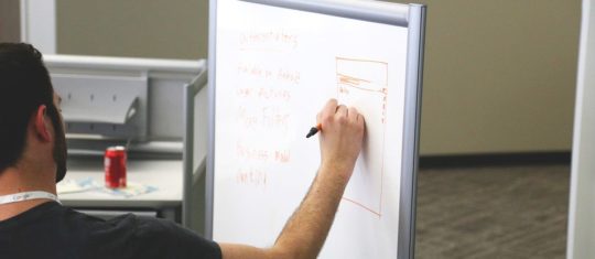 Personne écrivant sur un tableau pour planifier la gestion de projet